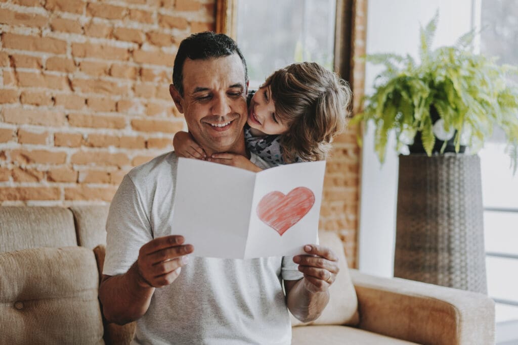 Kind knuddelt Vater. Vater hält Karte mit Herz in der Hand und lächelt