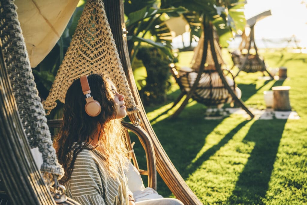 Lächelnde Frau mit Kopfhörer beim Hörbuchhören in der Natur im Hängesessel