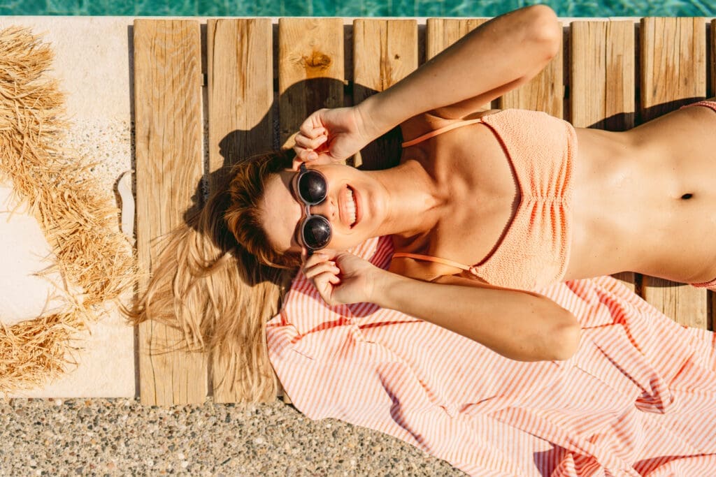 Frau in Bikini auf Steg mit Sonnenbrille, lachend