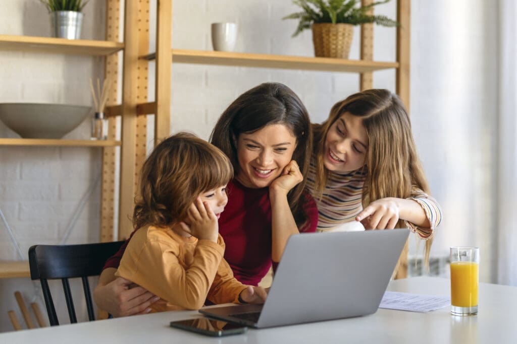 Boldog anyuka két gyermekkel a laptop előtt, a kiberzaklatás elleni védekezés jegyében